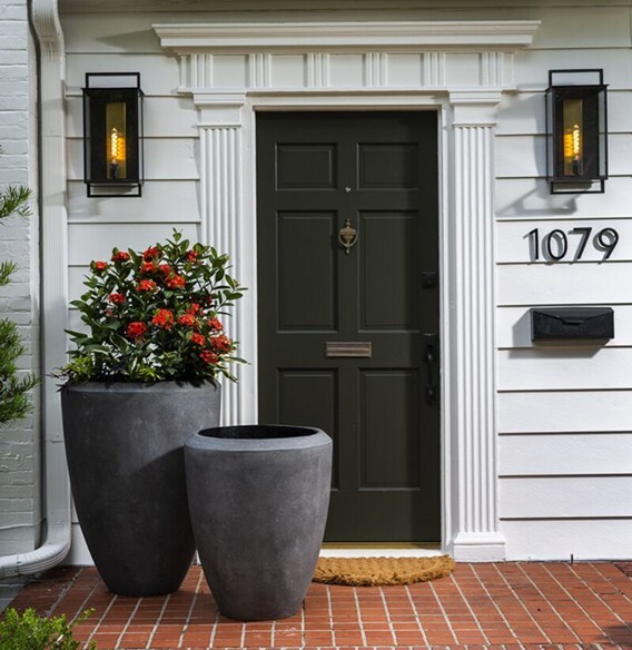 A front porch of a home painted white with tall planters to the left of front door